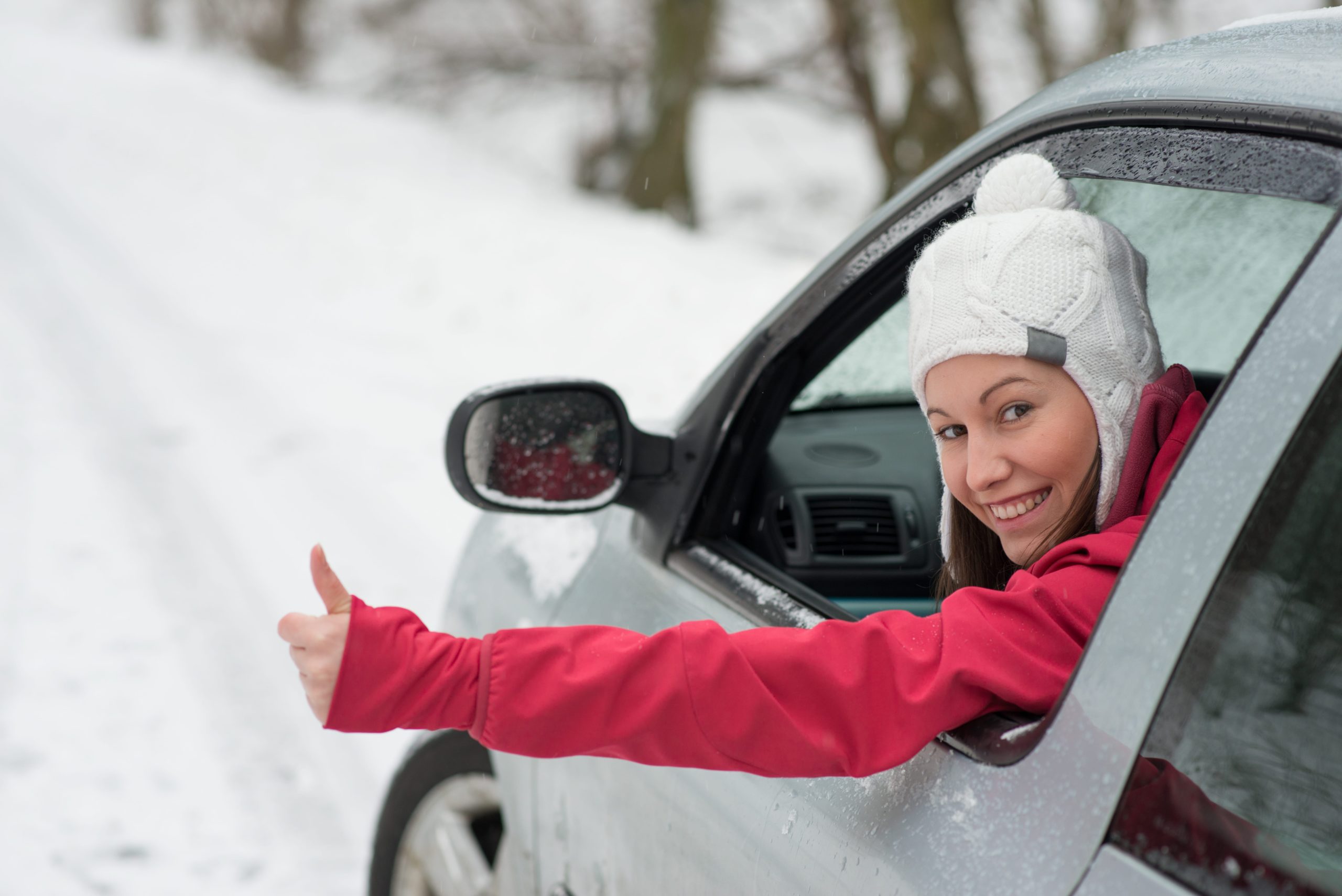 Woman driving car in snow and giving the thumbs up