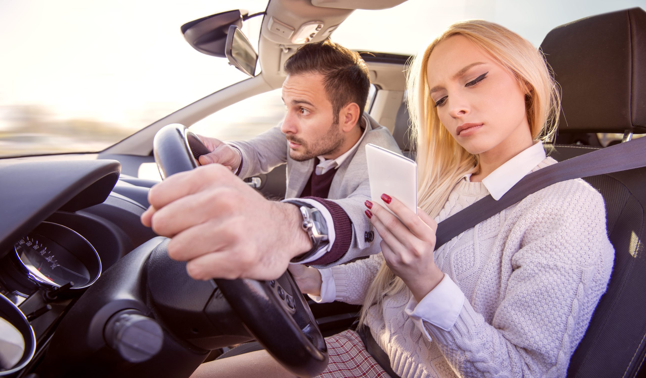 Woman driving while distracted as man grabs the steering wheel from her